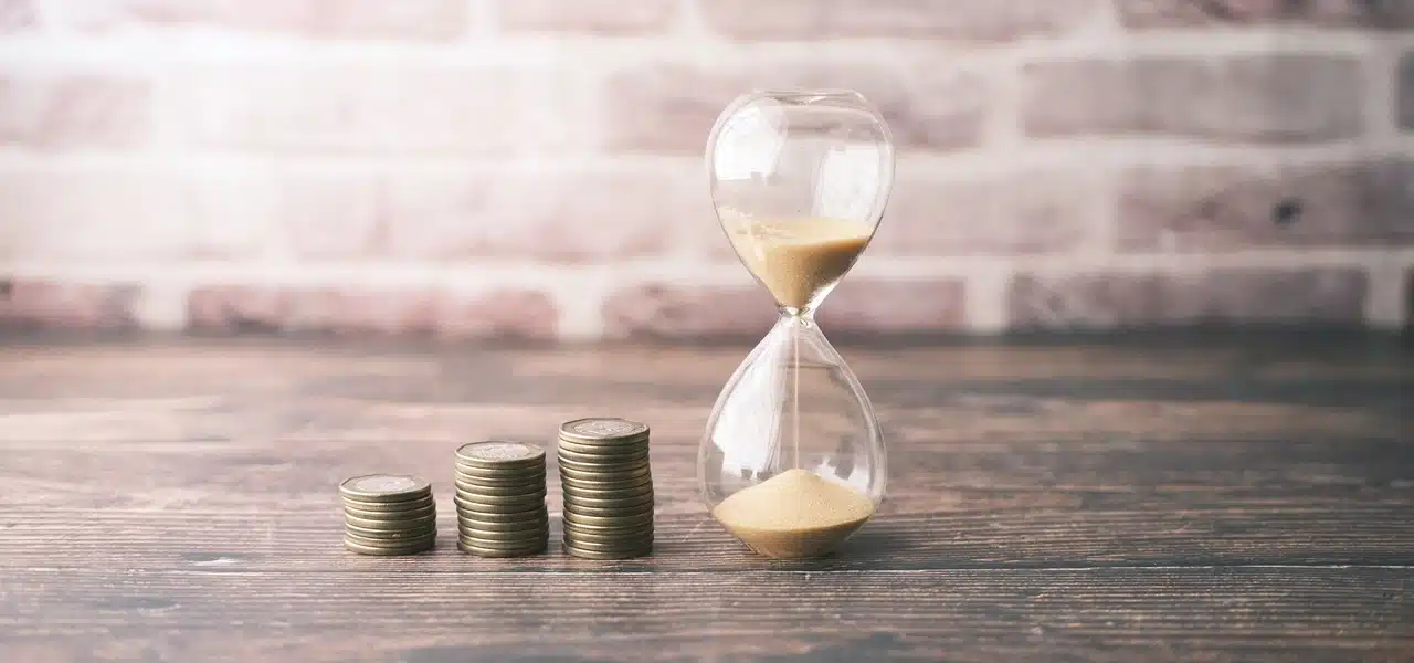 An hourglass beside stacks of coins