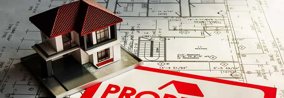 A house on top of architectural plans and a for sale sign