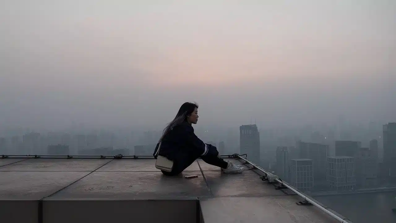 A photo of a woman sitting down on the edge of a city building rooftop pondering on the difference between Legal Separation, Annulment or Declaration of Nullity of Marriage