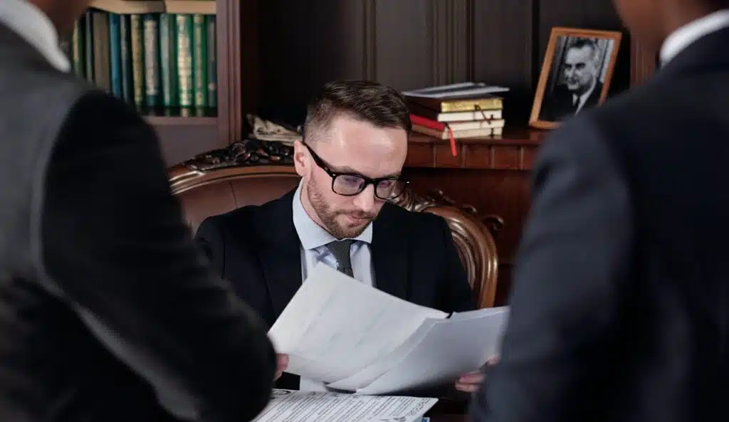 A lawyer sat at his desk checking the details of a Last Will and Testament with 2 people waiting. A Notarial Will Philippines does have advantages.
