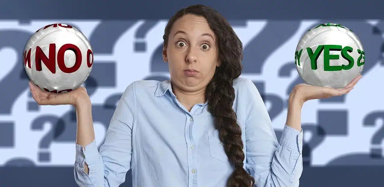 A confused looking woman in a blue shirt holding a ball with No written on it in her left hand and a ball with Yes on it in her right hand.